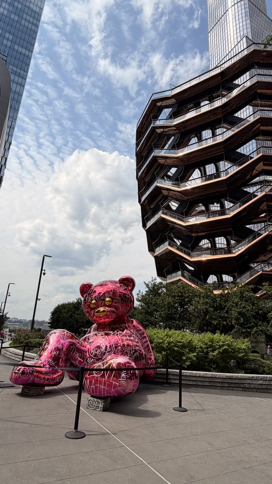 A bright pink graffiti-covered bear sculpture at Hudson Yards, standing out against The Vessel and surrounding towers.