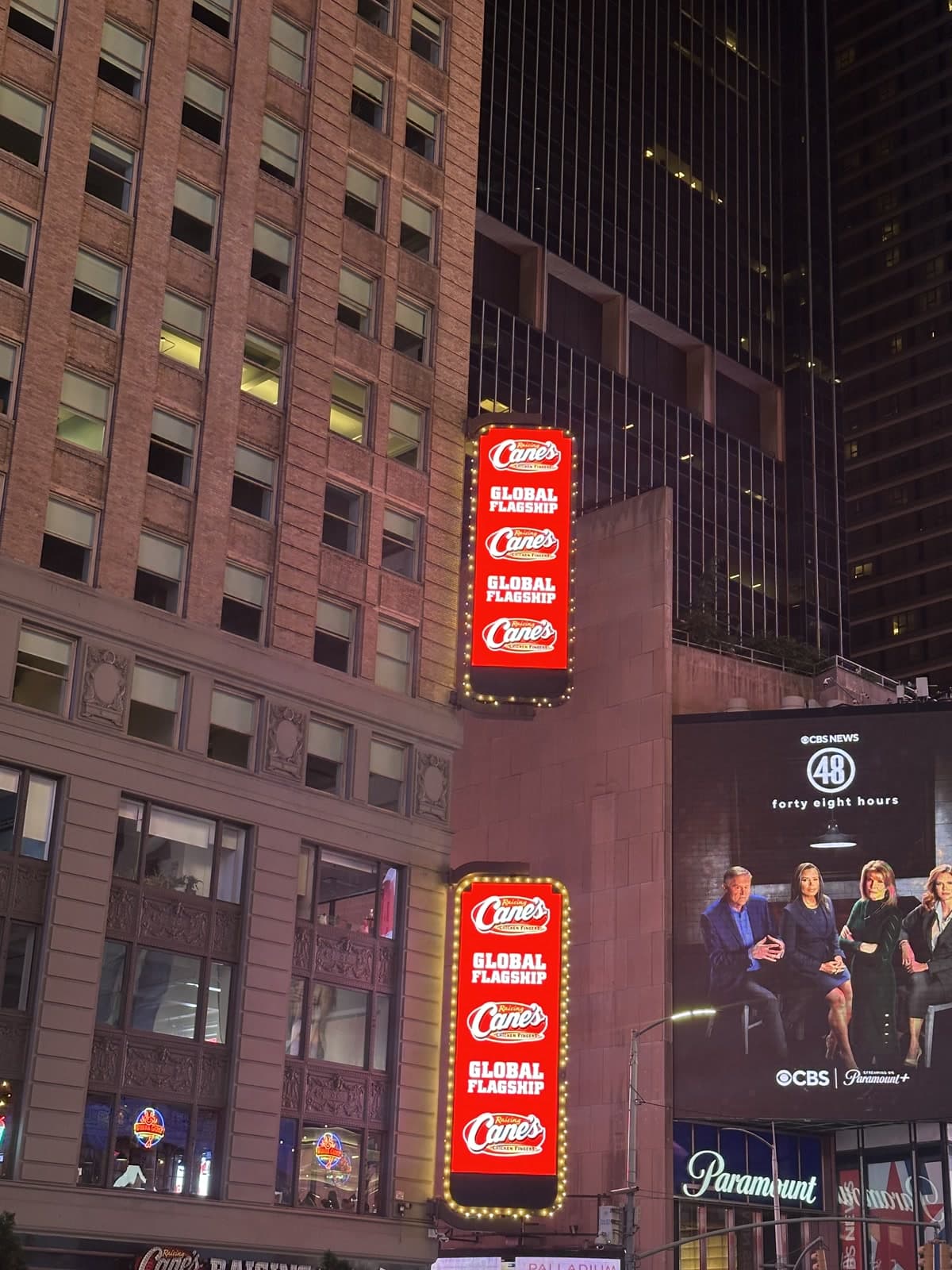 Raising Cane's Global Flagship signs stacked beside CBS and Paramount branding on a Times Square facade.