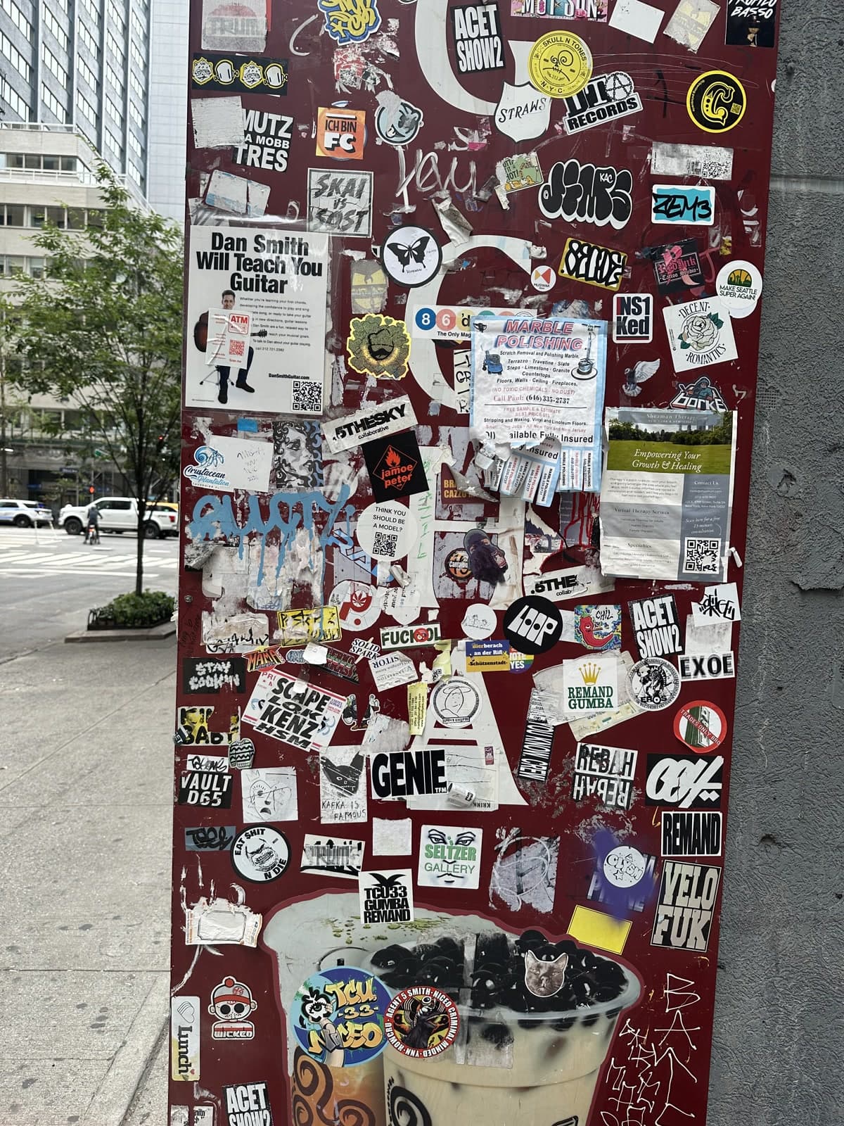 A city utility pillar covered in overlapping stickers, flyers, and logos competing for attention at street level.
