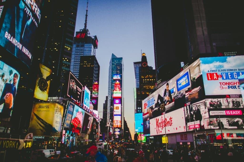 Looking up through Times Square at dusk, with dense crowds below and glowing billboards competing for attention on every building.