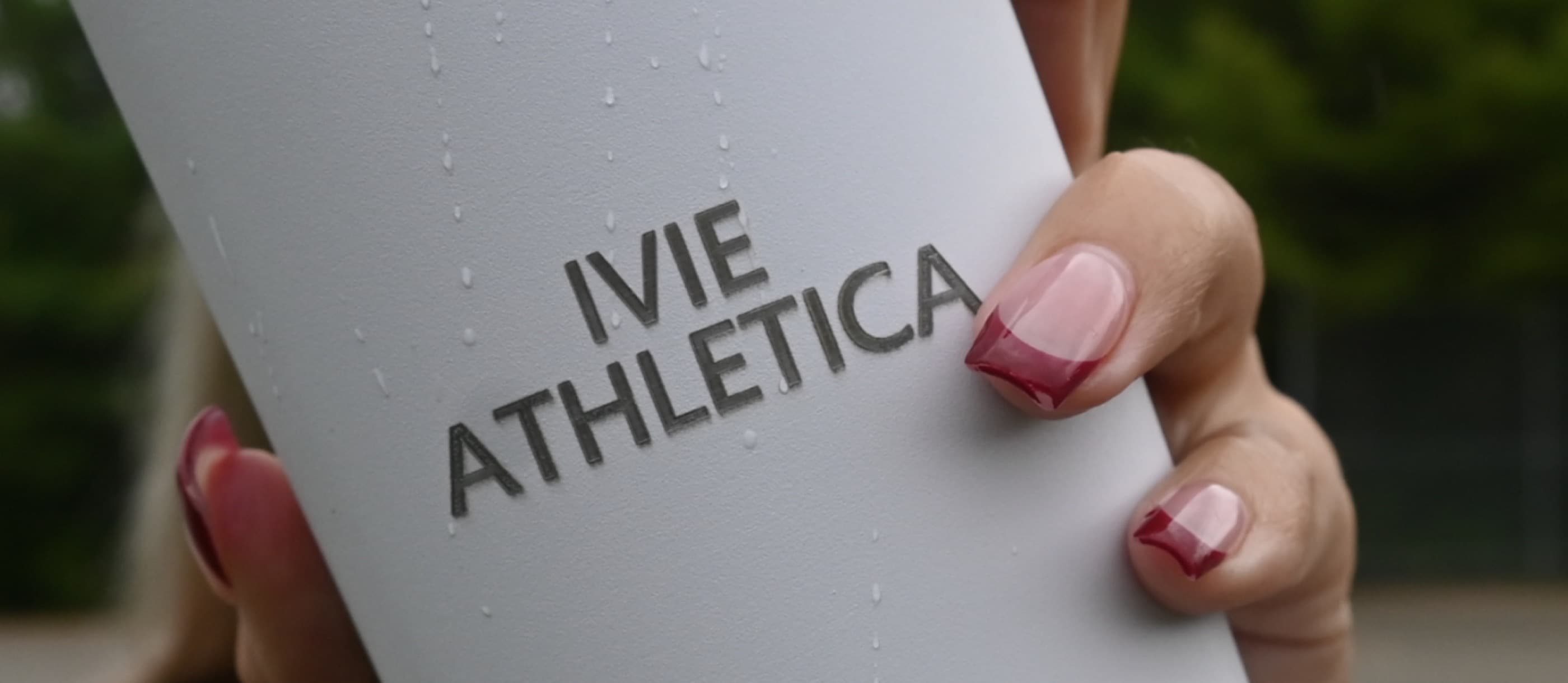 Hands holding an Ivie Athletica water bottle covered in condensation outdoors